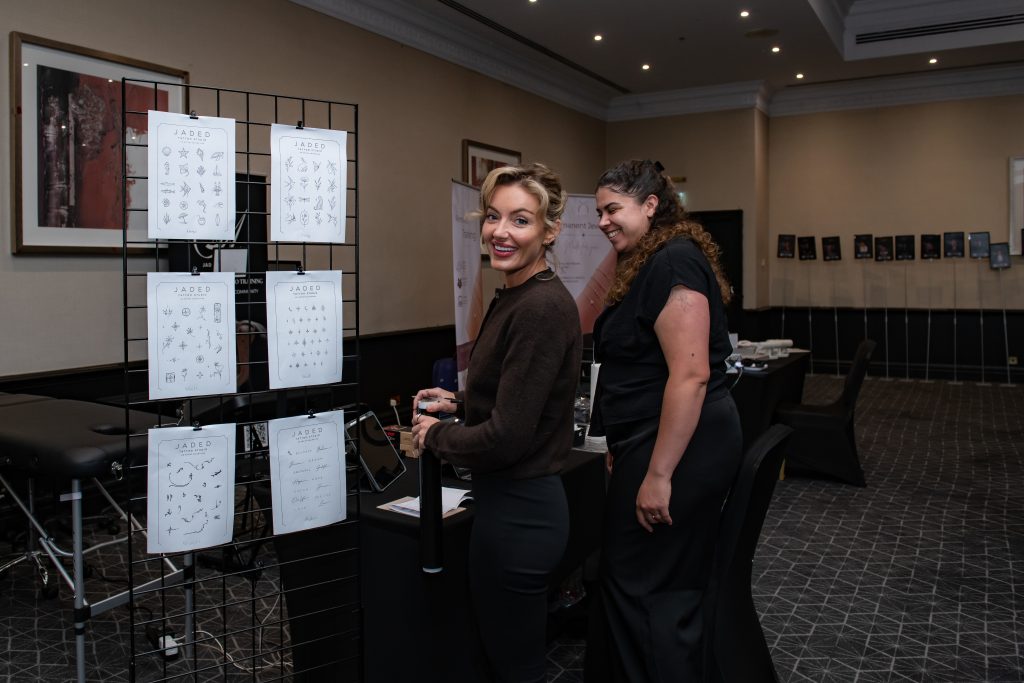 Two attendees in conversation beside boards of printed work at Queen's Night 2026.