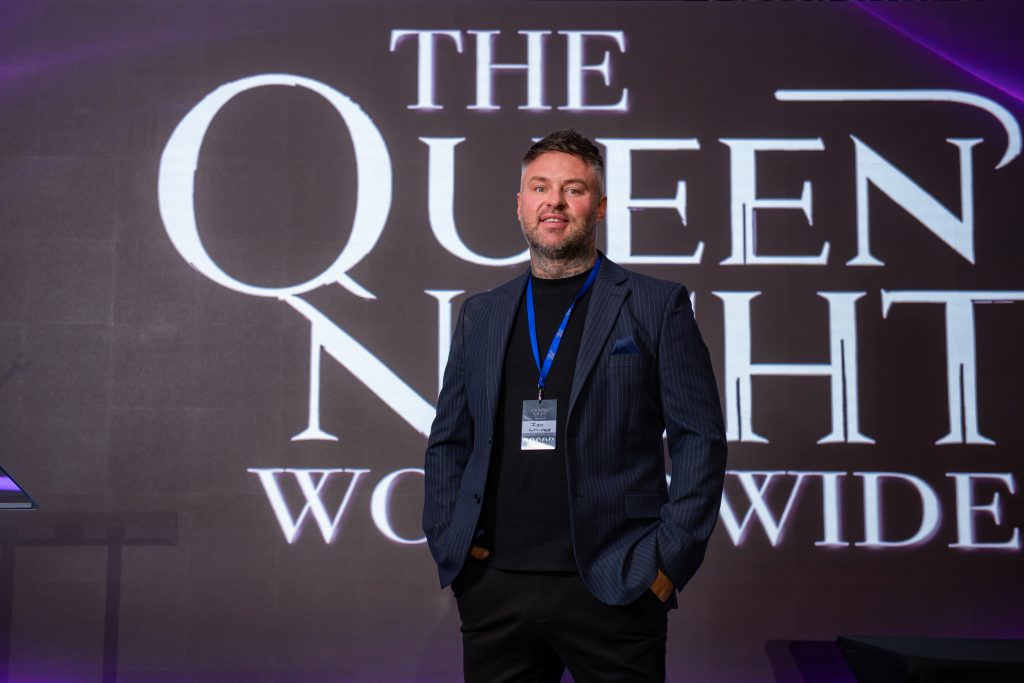 A person standing in front of the illuminated Queen's Night wordmark, 2026.