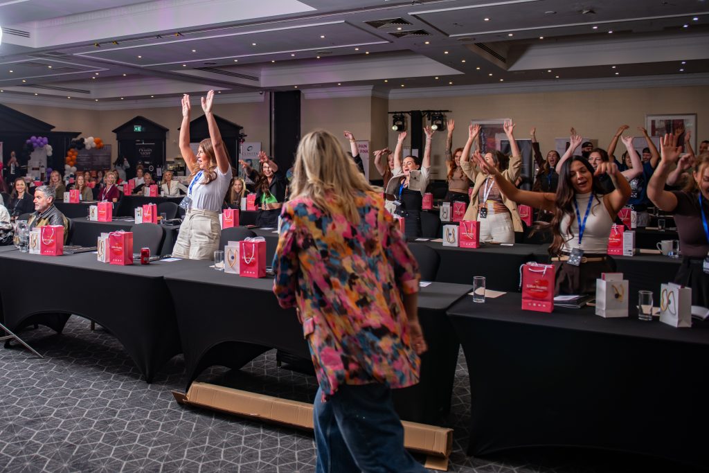 A room of seated attendees with their hands raised during a business session, a speaker walking between the tables.